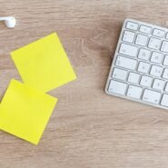 Post-it jaunes, clavier blanc et écouteurs sur un bureau en bois
