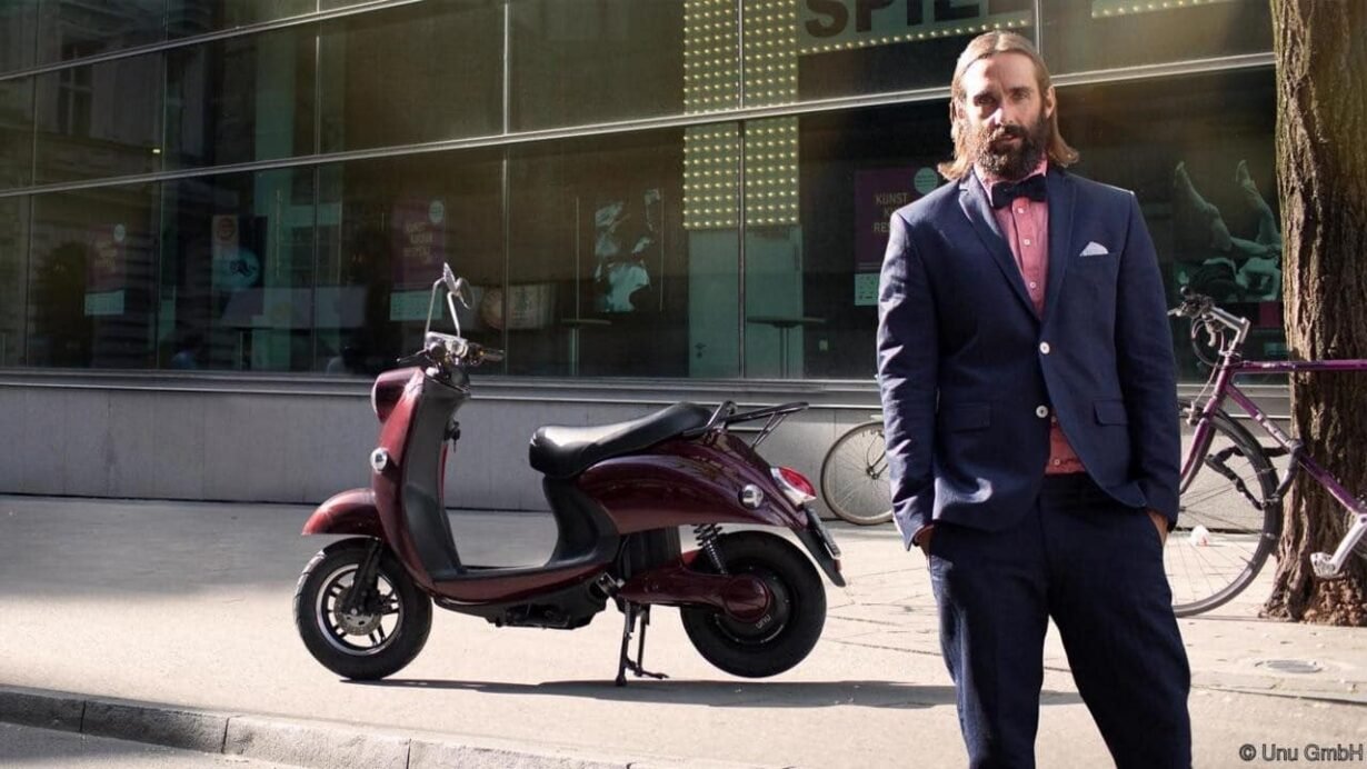 Homme en costume debout à côté d'un scooter électrique