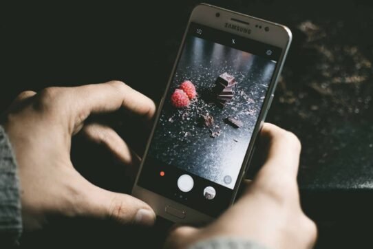 Main tenant un smartphone affichant des framboises et du chocolat