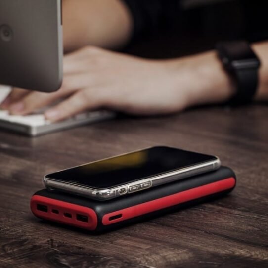 Smartphone posé sur un chargeur externe rouge et noir sur un bureau