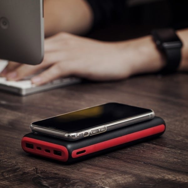 Smartphone posé sur un chargeur externe rouge et noir sur un bureau