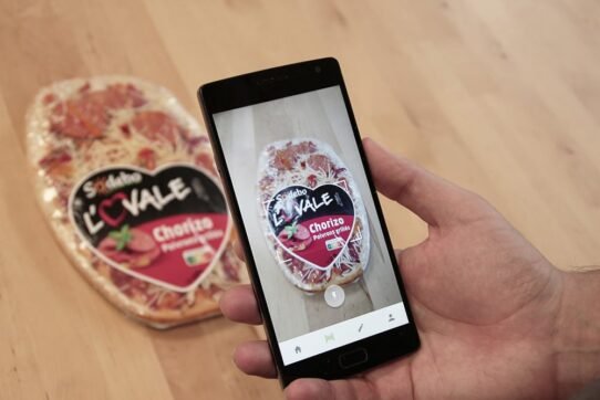 Main tenant un smartphone scannant une pizza emballée