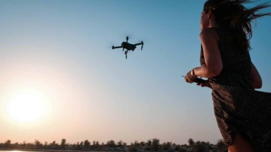 Femme contrôlant un drone sous un ciel bleu au coucher de soleil
