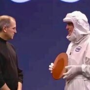 Deux hommes sur scène, l'un en combinaison, tenant un objet circulaire