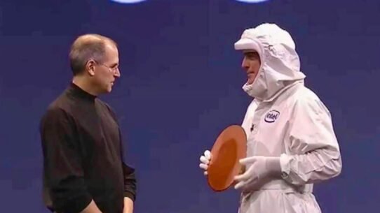 Deux hommes sur scène, l'un en combinaison, tenant un objet circulaire