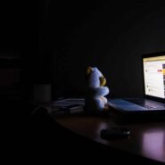 Un ours en peluche regarde un ordinateur portable allumé sur une table