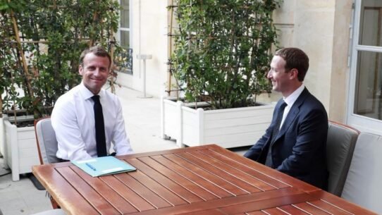 Deux hommes en costume discutent autour d'une table en bois à l'extérieur