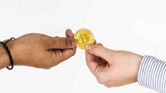 Deux mains échangent une pièce de bitcoin dorée