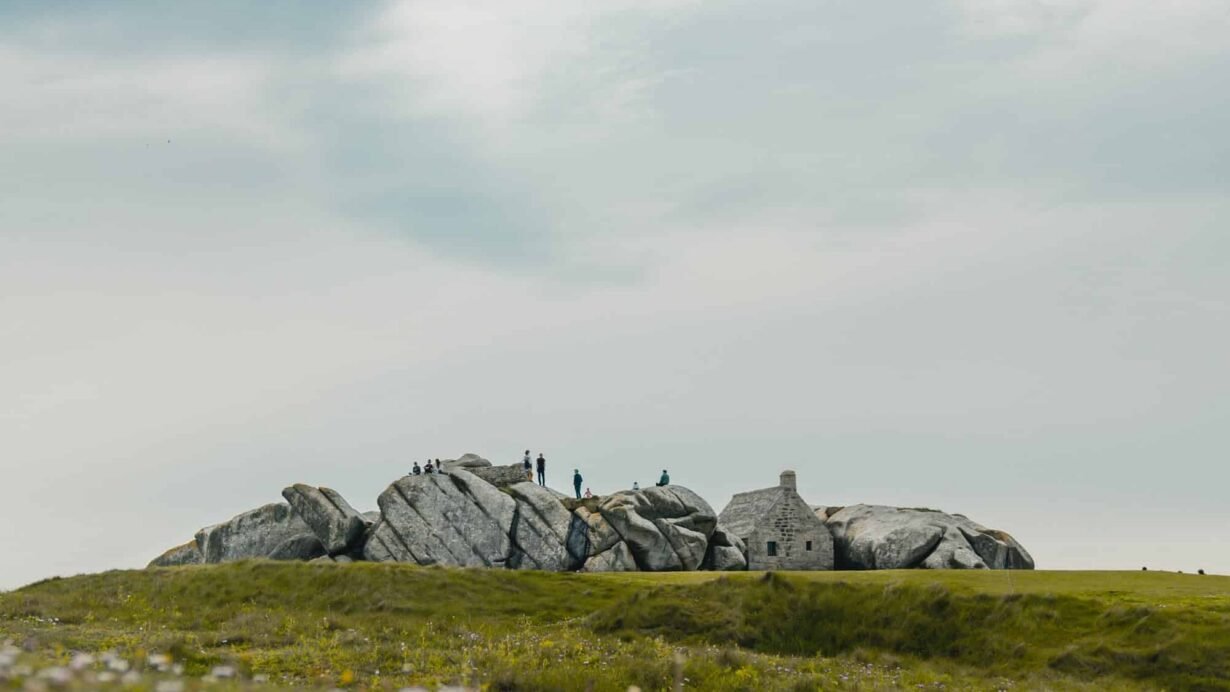 Maison en pierre entourée de rochers sur une colline fleurie