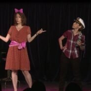 Deux femmes sur scène dans un sketch humoristique avec accessoires