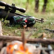 Haut-parleur camouflage à côté d'une carabine sur l'herbe