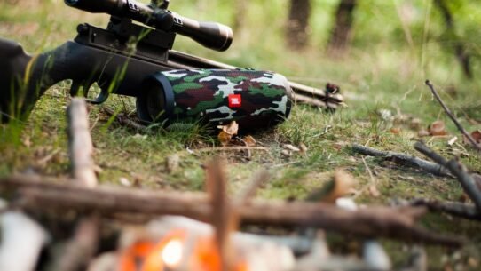 Haut-parleur camouflage à côté d'une carabine sur l'herbe