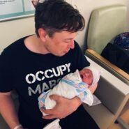 Homme assis tenant un bébé emmailloté dans ses bras