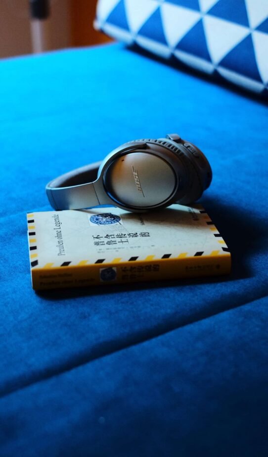 Casque audio gris posé sur un livre jaune sur un canapé bleu