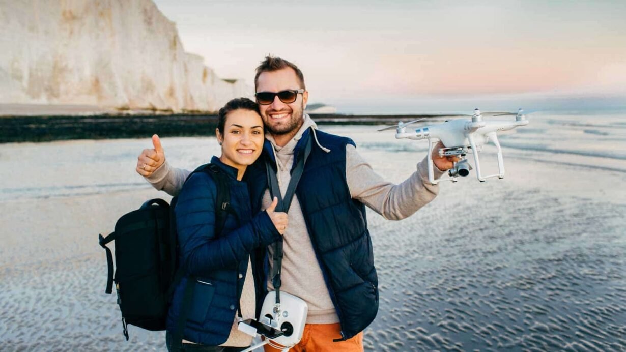 Couple souriant sur la plage avec un drone en main