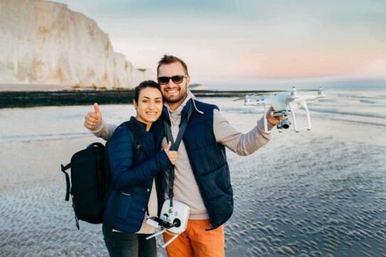 Couple souriant sur la plage avec un drone en main