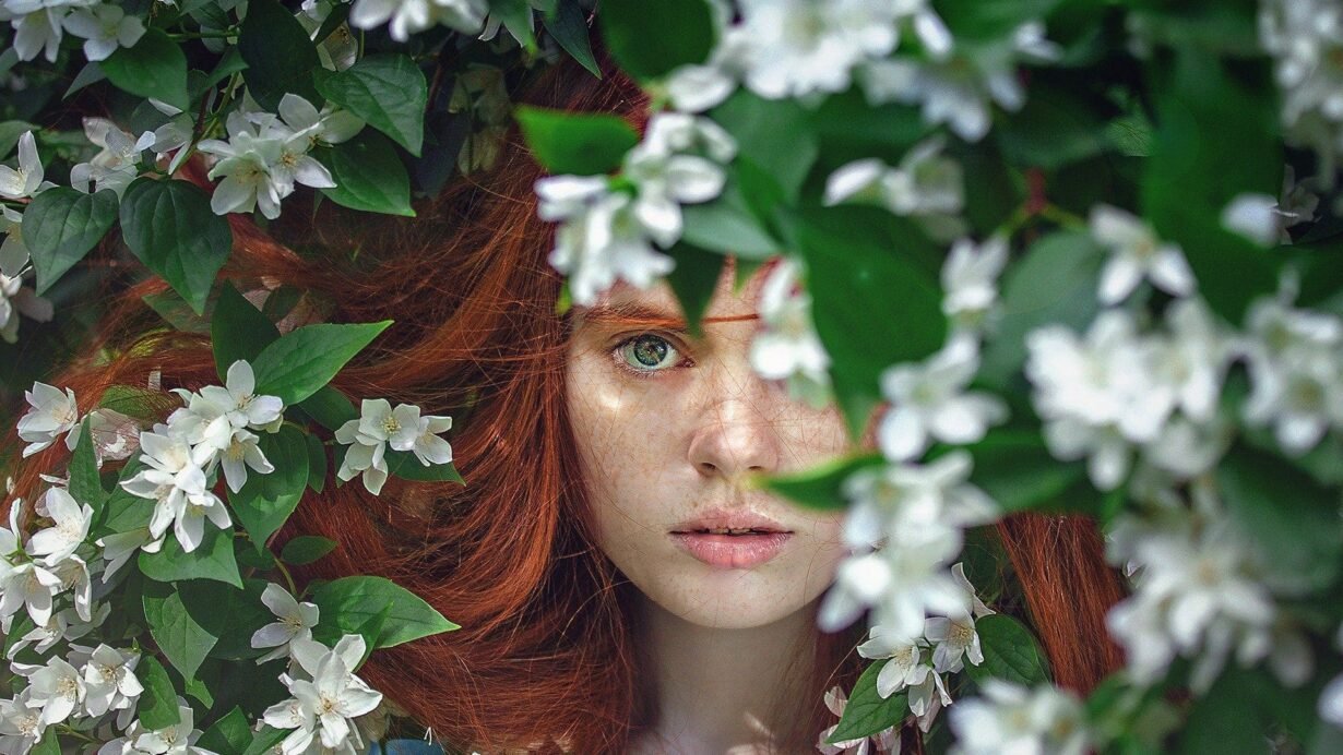 Visage de femme rousse entouré de fleurs blanches