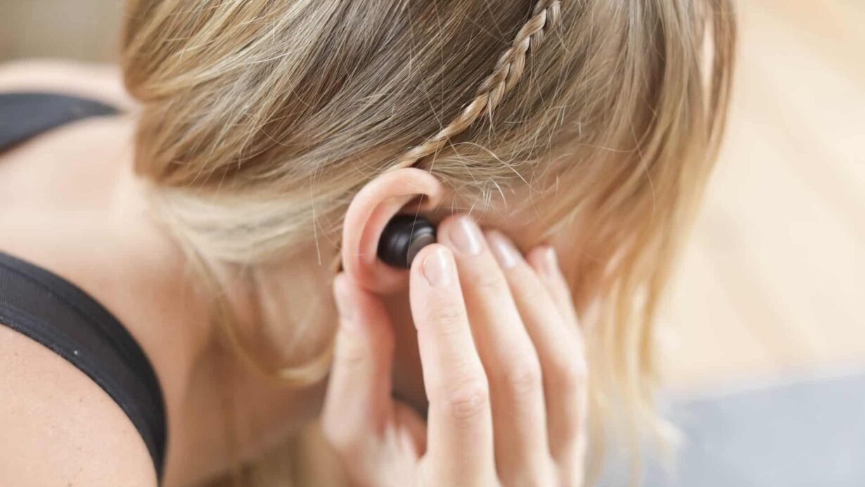 Femme blonde ajustant un écouteur sans fil dans son oreille