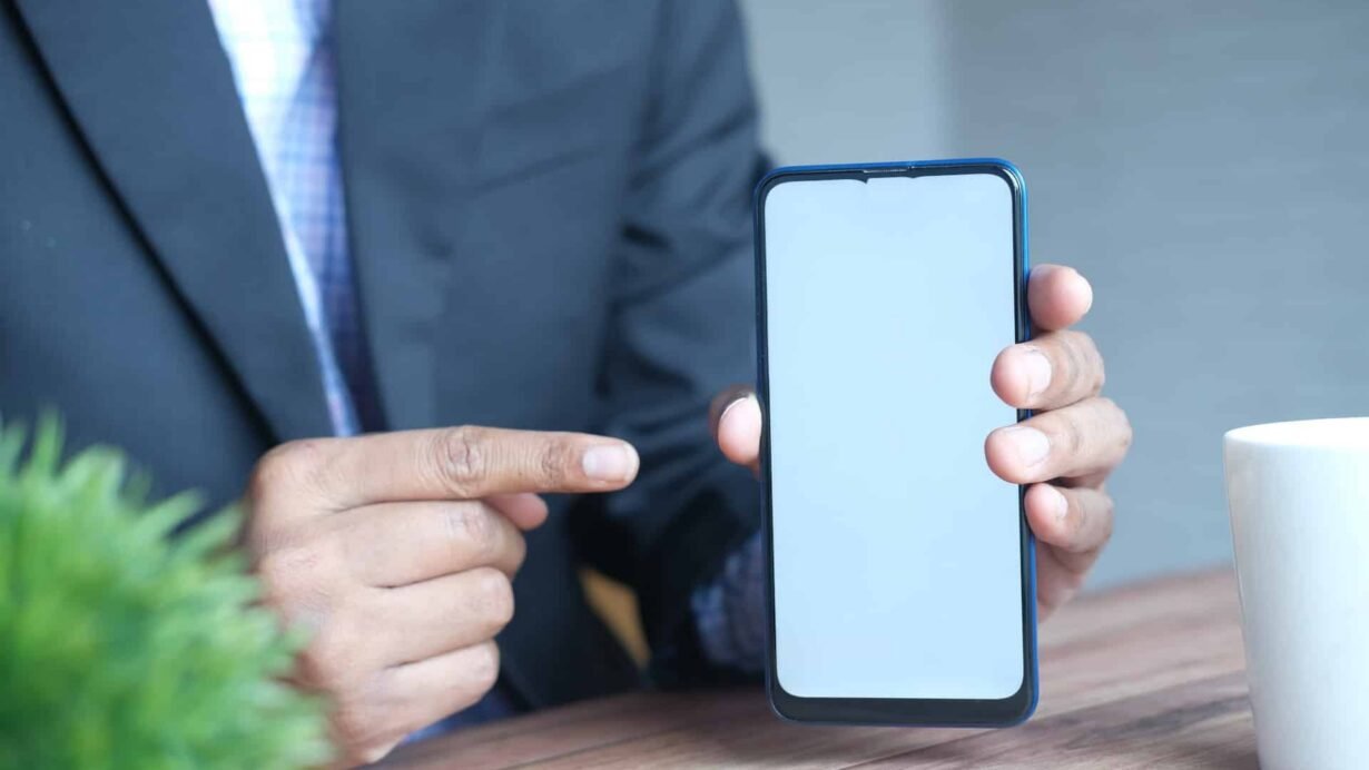 Main tenant un smartphone avec écran vide sur une table en bois