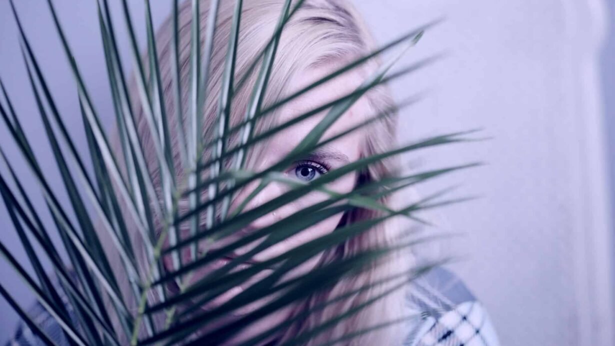 Femme blonde cachée derrière des feuilles de palmier