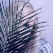 Femme blonde cachée derrière des feuilles de palmier