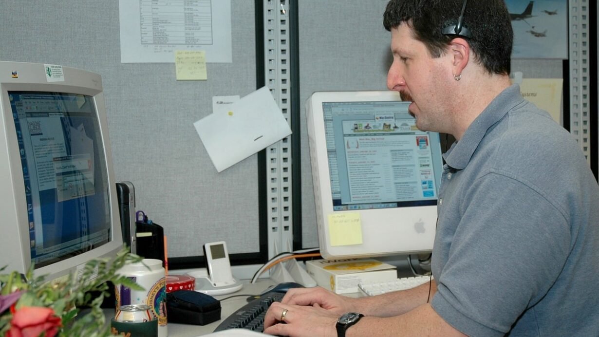 Homme concentré sur deux écrans d'ordinateur dans un bureau