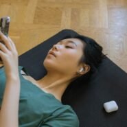 Personne allongée sur un tapis de yoga utilisant un smartphone avec écouteurs