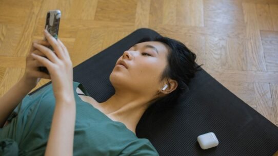 Personne allongée sur un tapis de yoga utilisant un smartphone avec écouteurs