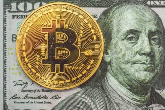 Pièce de bitcoin sur fond de billet de 100 dollars