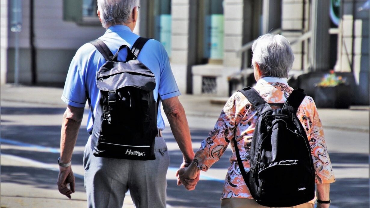 Couple de seniors avec sacs à dos marchant en ville main dans la main