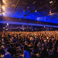 Une foule assiste à une conférence dans une salle illuminée