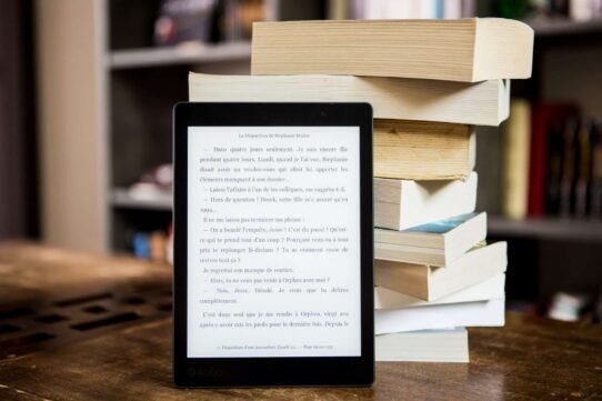 Tablette de lecture numérique devant une pile de livres en papier