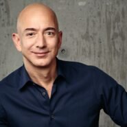 Homme chauve en chemise noire souriant devant un mur en béton