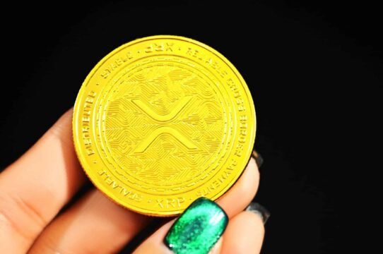 Gros plan sur une pièce de cryptomonnaie XRP dorée tenue par une main