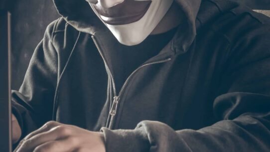 Personne masquée en hoodie tapant sur un ordinateur portable