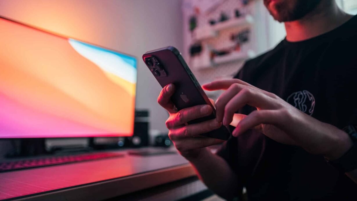 Homme utilisant un smartphone devant un écran d'ordinateur lumineux