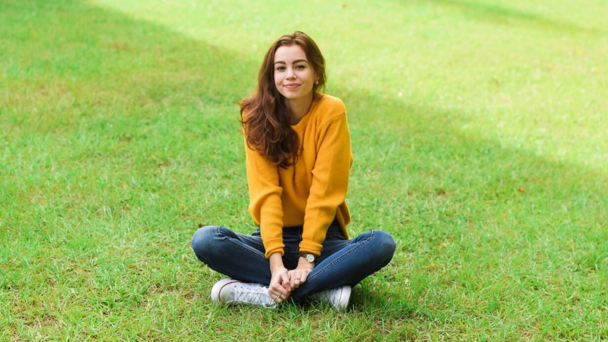 Femme en pull jaune assise en tailleur sur l'herbe
