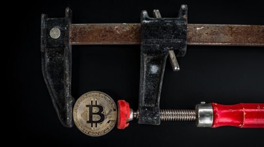 Pièce de Bitcoin serrée dans un étau en métal