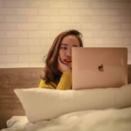 Femme en pull jaune utilisant un ordinateur portable au lit