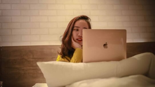 Femme en pull jaune utilisant un ordinateur portable au lit