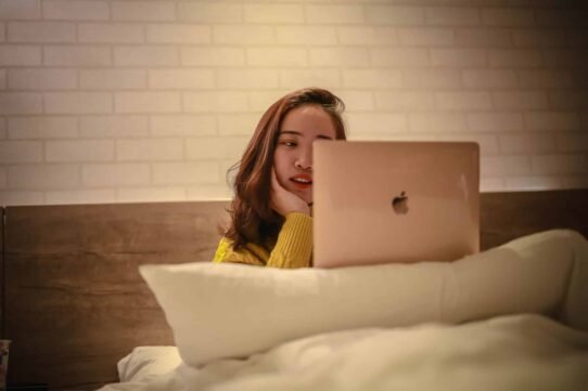 Femme en pull jaune utilisant un ordinateur portable au lit