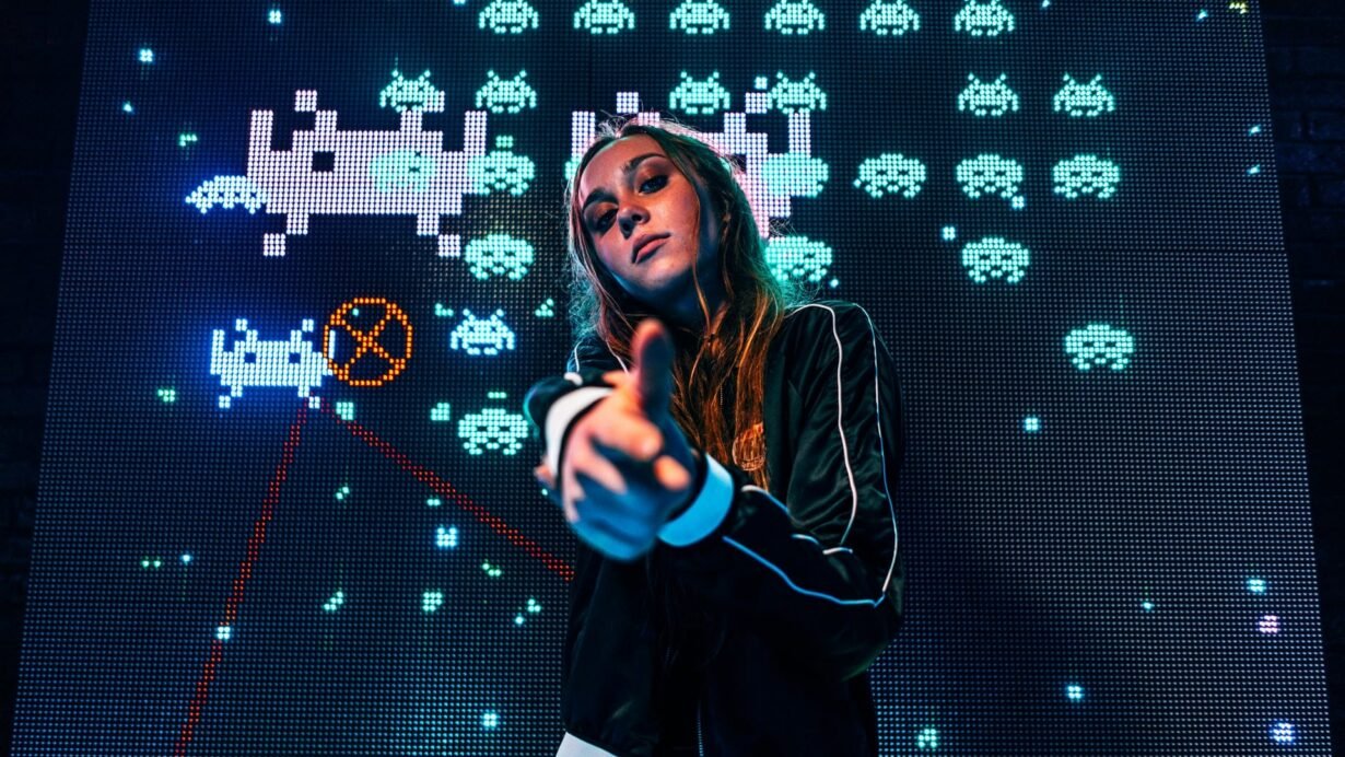 Femme posant devant un écran affichant un jeu vidéo rétro