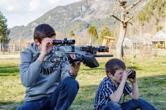 Deux enfants jouent en plein air avec des jumelles et un fusil jouet