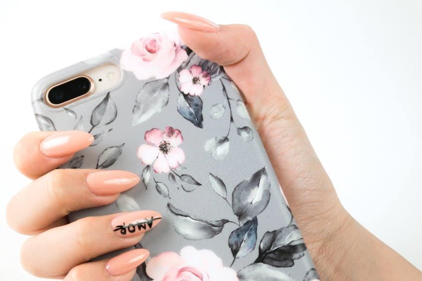 Main tenant une coque de téléphone à motifs floraux roses et gris