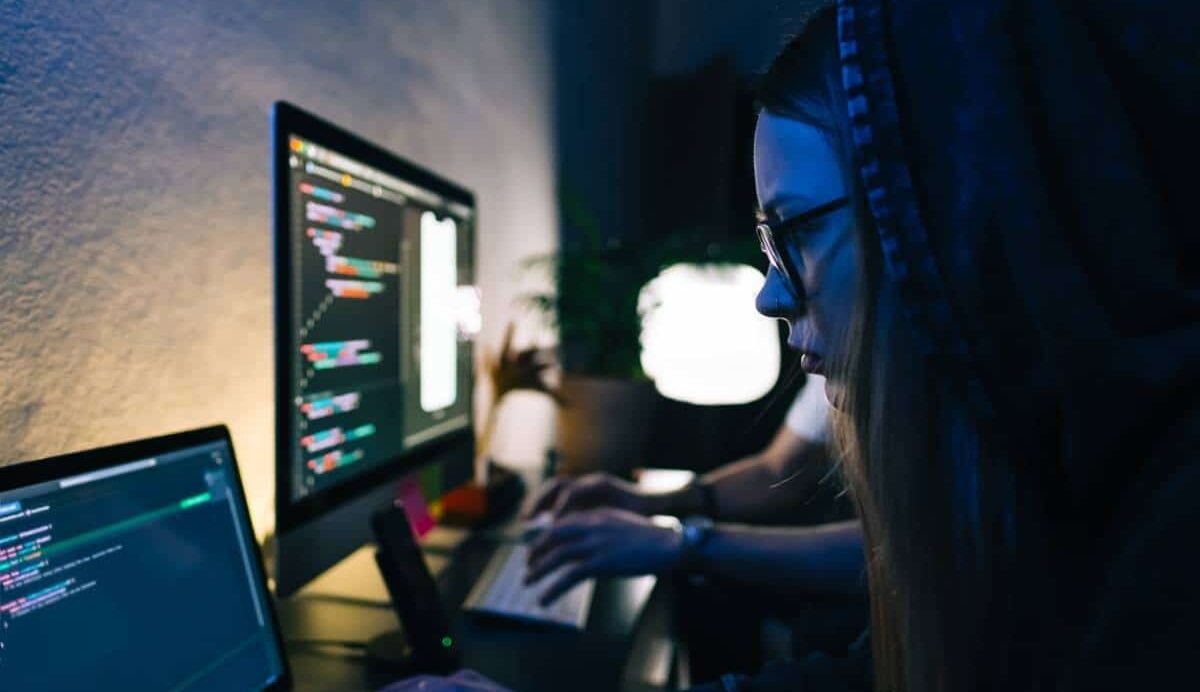 Deux personnes codant sur des ordinateurs dans un environnement sombre