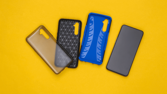 Trois étuis de smartphone colorés à côté d'un téléphone sur fond jaune