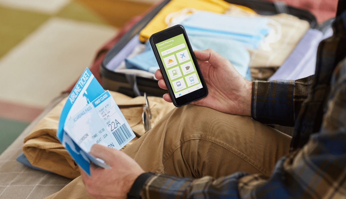 Personne tenant un billet d'avion et un smartphone devant une valise ouverte