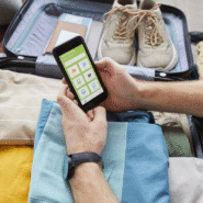 Personne utilisant une application de voyage devant une valise ouverte