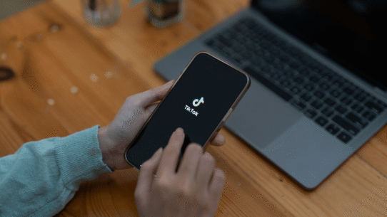 Personne utilisant TikTok sur un smartphone avec un ordinateur portable à proximité