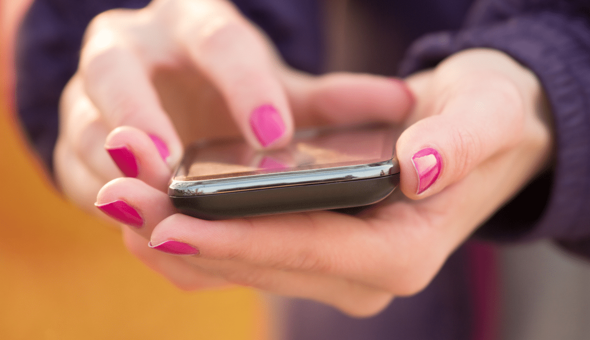 Personne utilisant un smartphone avec vernis à ongles rose